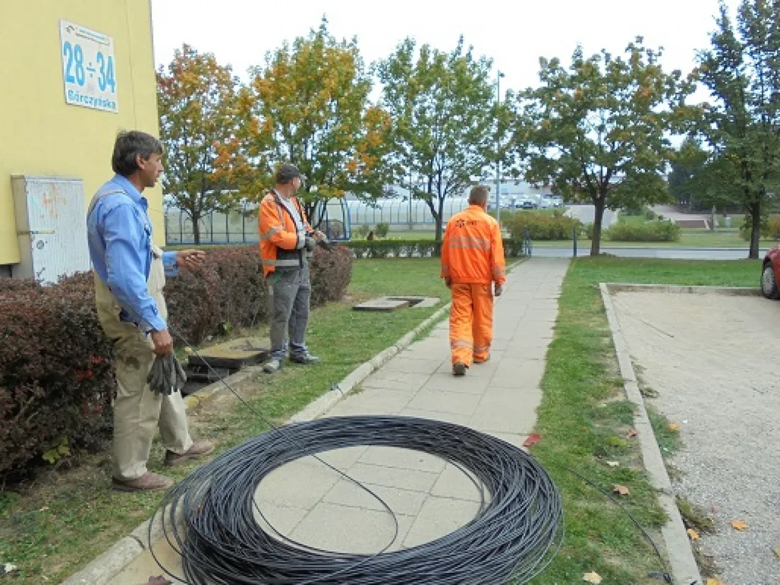 Krąg kabla światłowodowego na trawniku przy chodniku, ekipa w tle