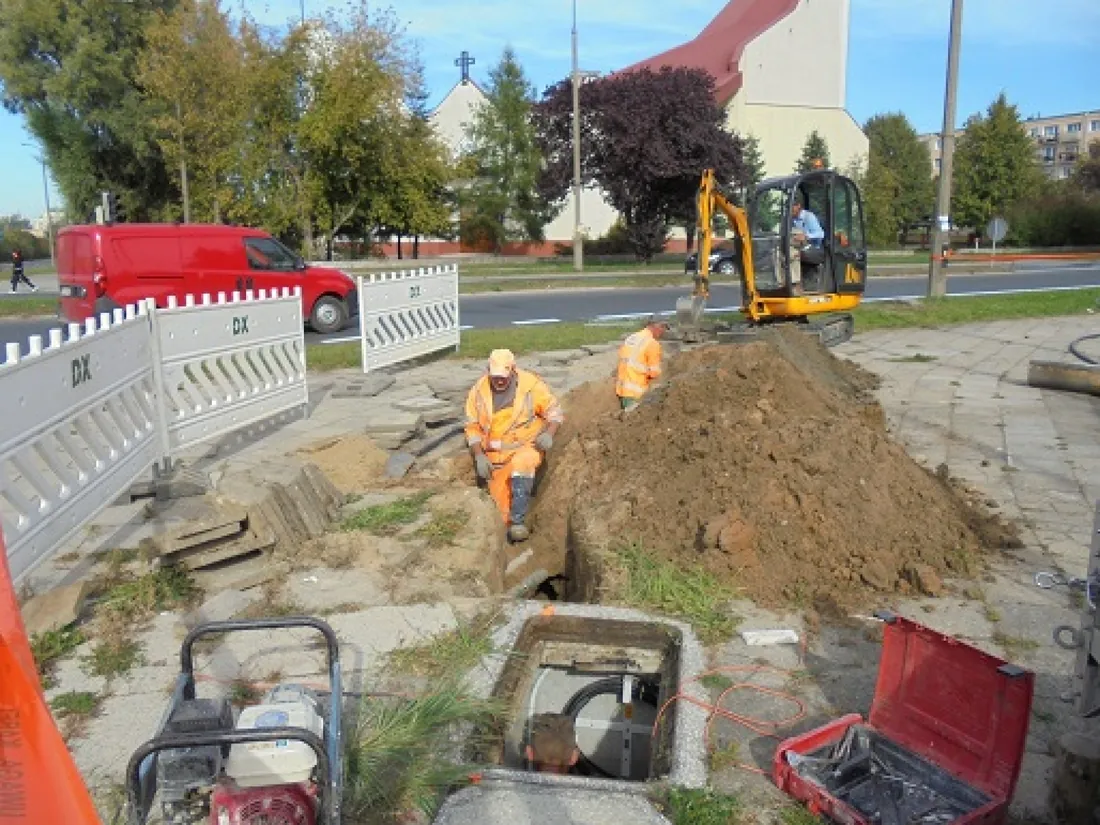 Wykop pod kanalizację wzdłuż ulicy, minikoparka w tle